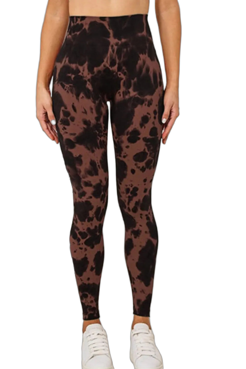 High-waist brown leggings with black tie-dye splotches worn with white sneakers, model's hands at sides, black background