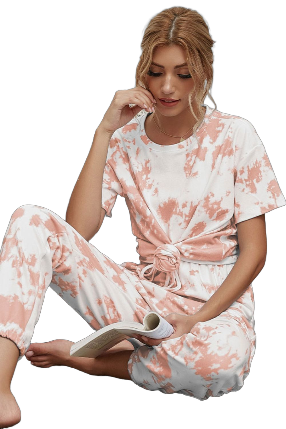 Seated woman wearing peach-and-white tie-dye short-sleeve tee knotted at the waist and matching drawstring joggers, holding…