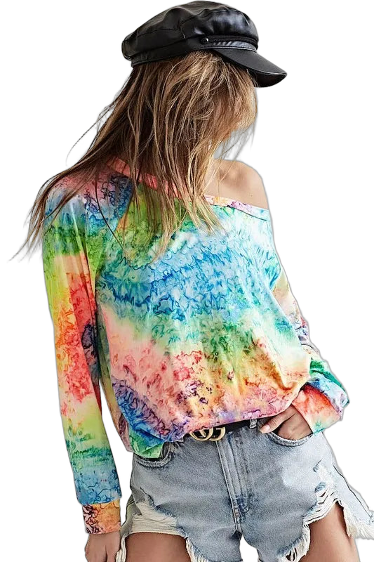 Woman wearing multicolor tie-dye long-sleeve off-shoulder top, light-wash ripped denim shorts, black leather cap.