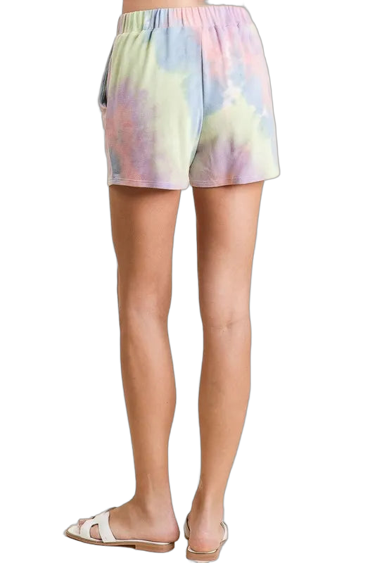 Back view of pastel tie-dye elastic-waist shorts with side pockets, worn with white slide sandals