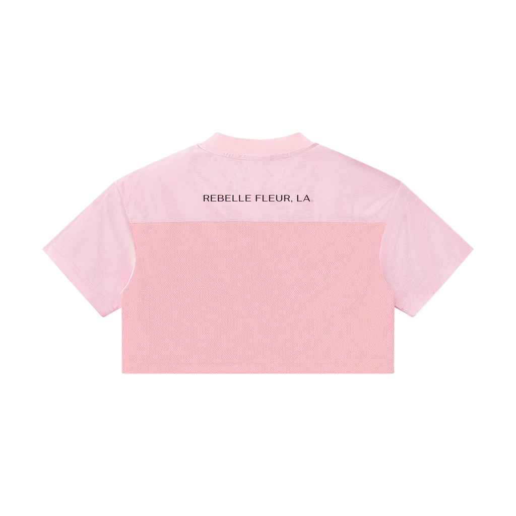 Back of cropped pink paneled jersey with short sleeves and 'REBELLE FLEUR, LA' text across upper back