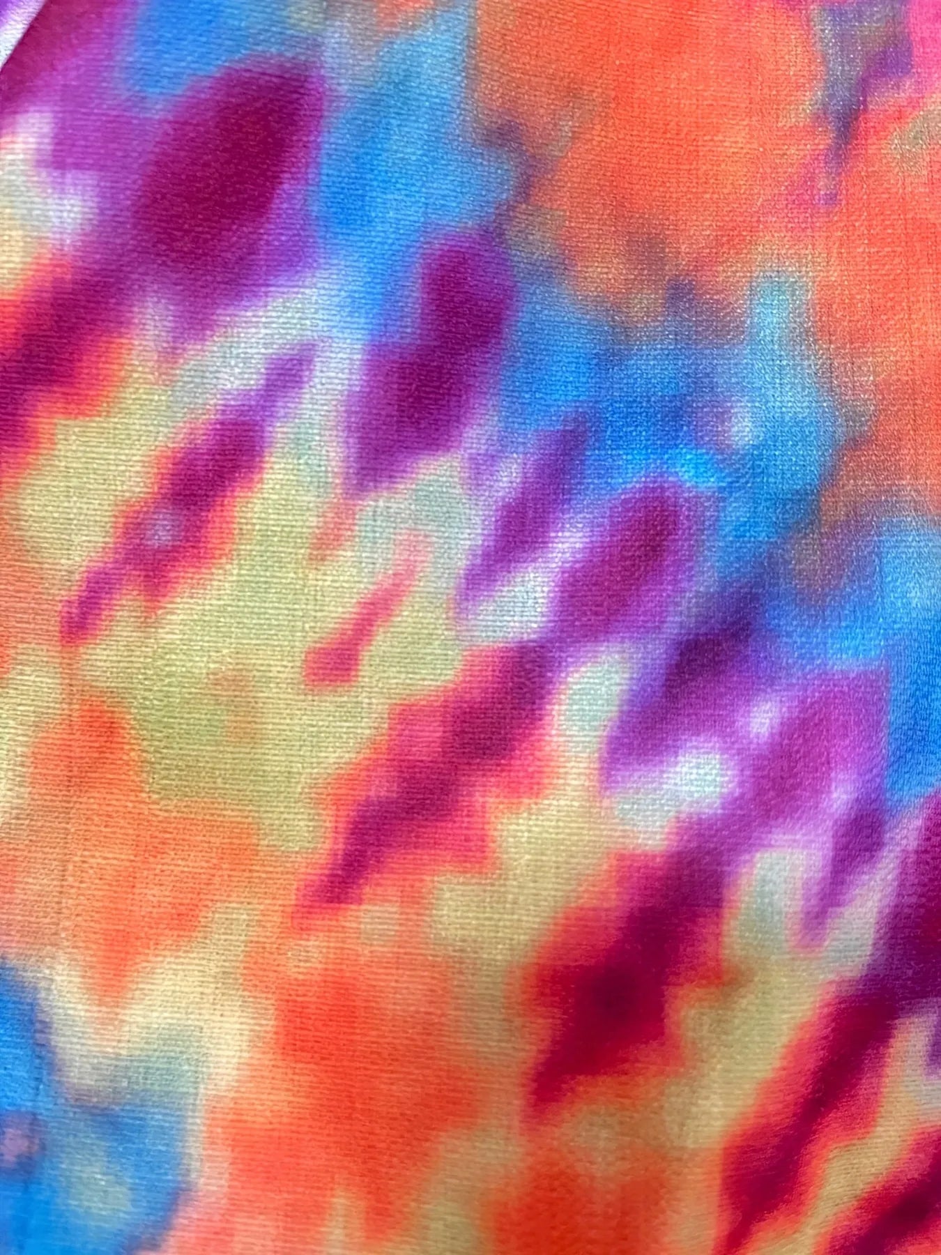 Close-up tie-dye fabric with swirls of purple, blue, orange, pink and yellow, visible knit texture