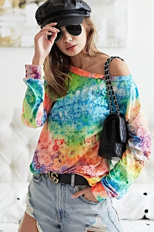 Off-shoulder long-sleeve tie-dye top with multicolor swirls, distressed denim shorts and chain-strap shoulder bag