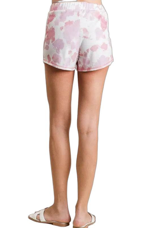 Rear view of women's light pink tie-dye shorts with elastic waistband and curved hem, worn with sandals.