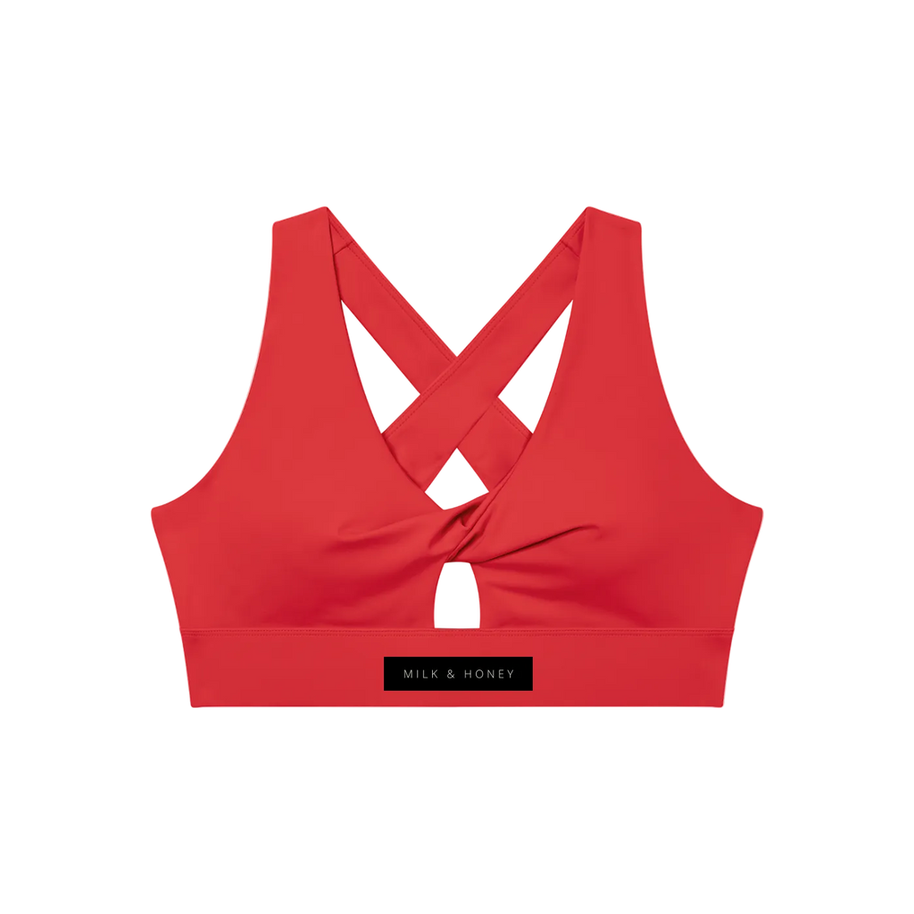 Red twist-front sports bra with crisscross back, small front keyhole and wide elastic band labeled "MILK & HONEY"