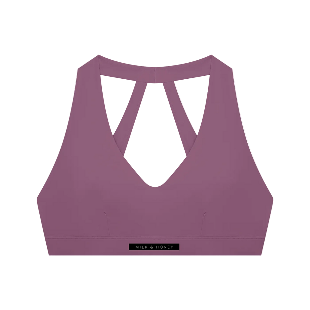 Plum purple cropped sports bra with deep V-front, crossed-back straps and elastic underband labeled 'MILK & HONEY'.
