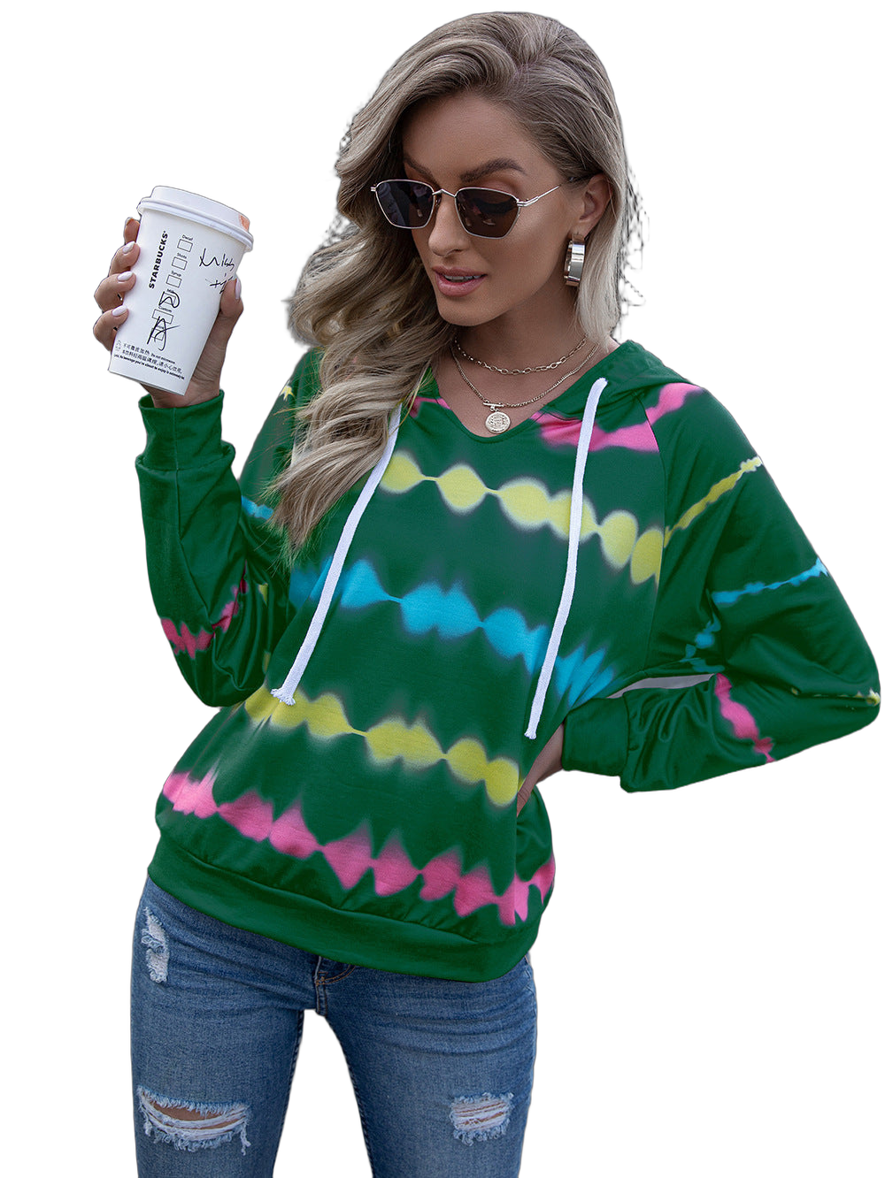 Woman wearing green tie-dye hooded sweatshirt with white drawstrings, sunglasses, ripped jeans, holding a takeaway coffee cup