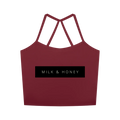 Cropped red tank with thin crossed racerback straps and centered black rectangle reading 'MILK & HONEY'.