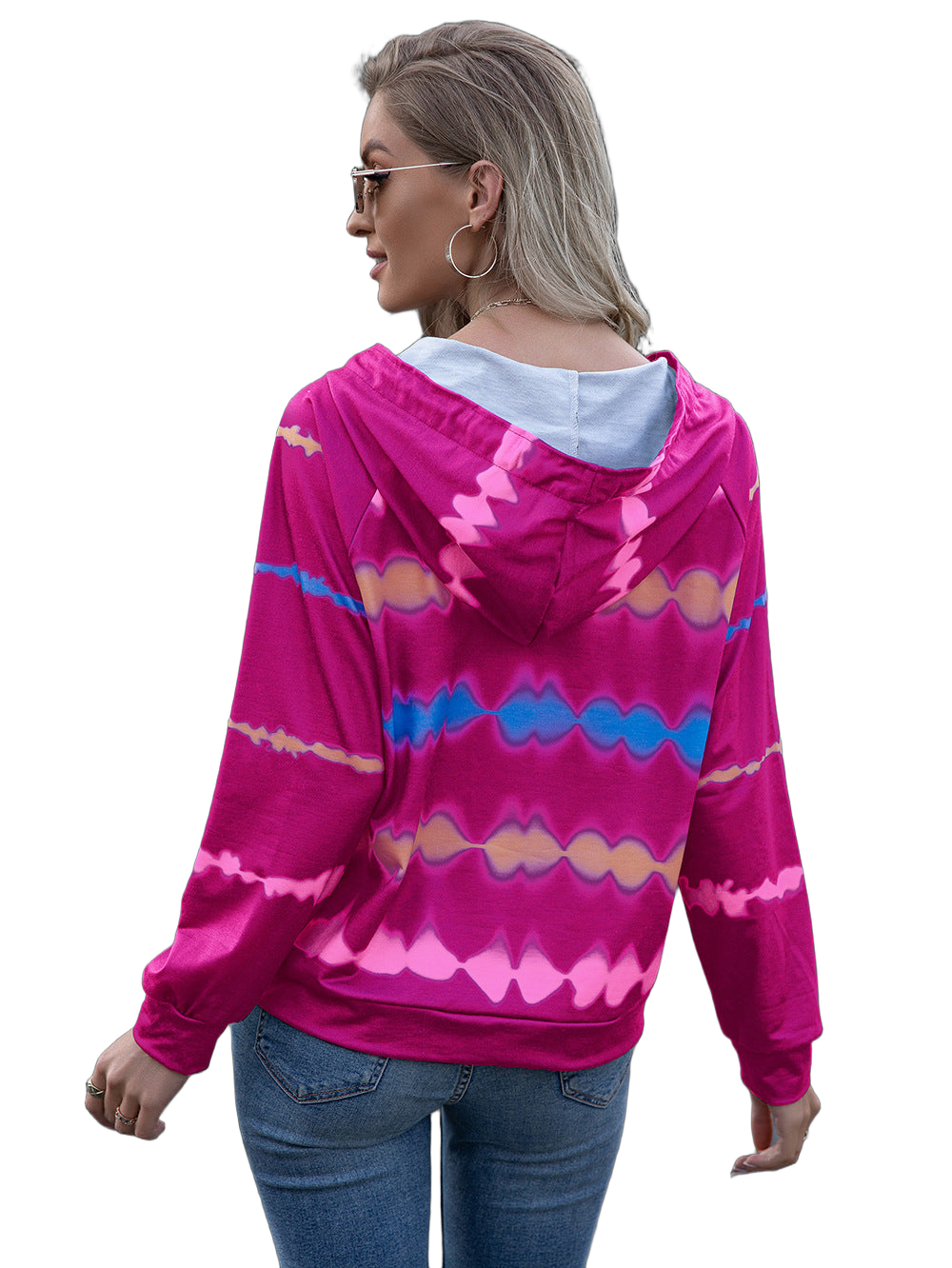 Back view of woman wearing hot-pink tie-dye hooded raglan hoodie with light hood lining, hoop earring, and jeans