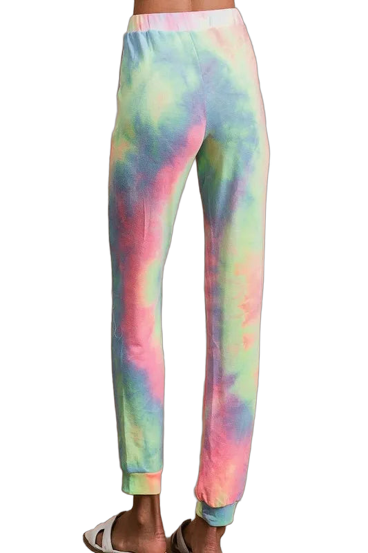 Back view of pastel tie-dye pants with elastic waistband, tapered legs and cuffed ankles; model wearing white slide sandals