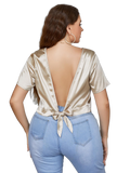 Back view of plus-size model wearing gold short-sleeve cropped blouse with deep V back tied in a bow over light-wash jeans