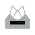 Gray crop sports bra with thin crisscross back straps and black MILK & HONEY rectangular logo panel
