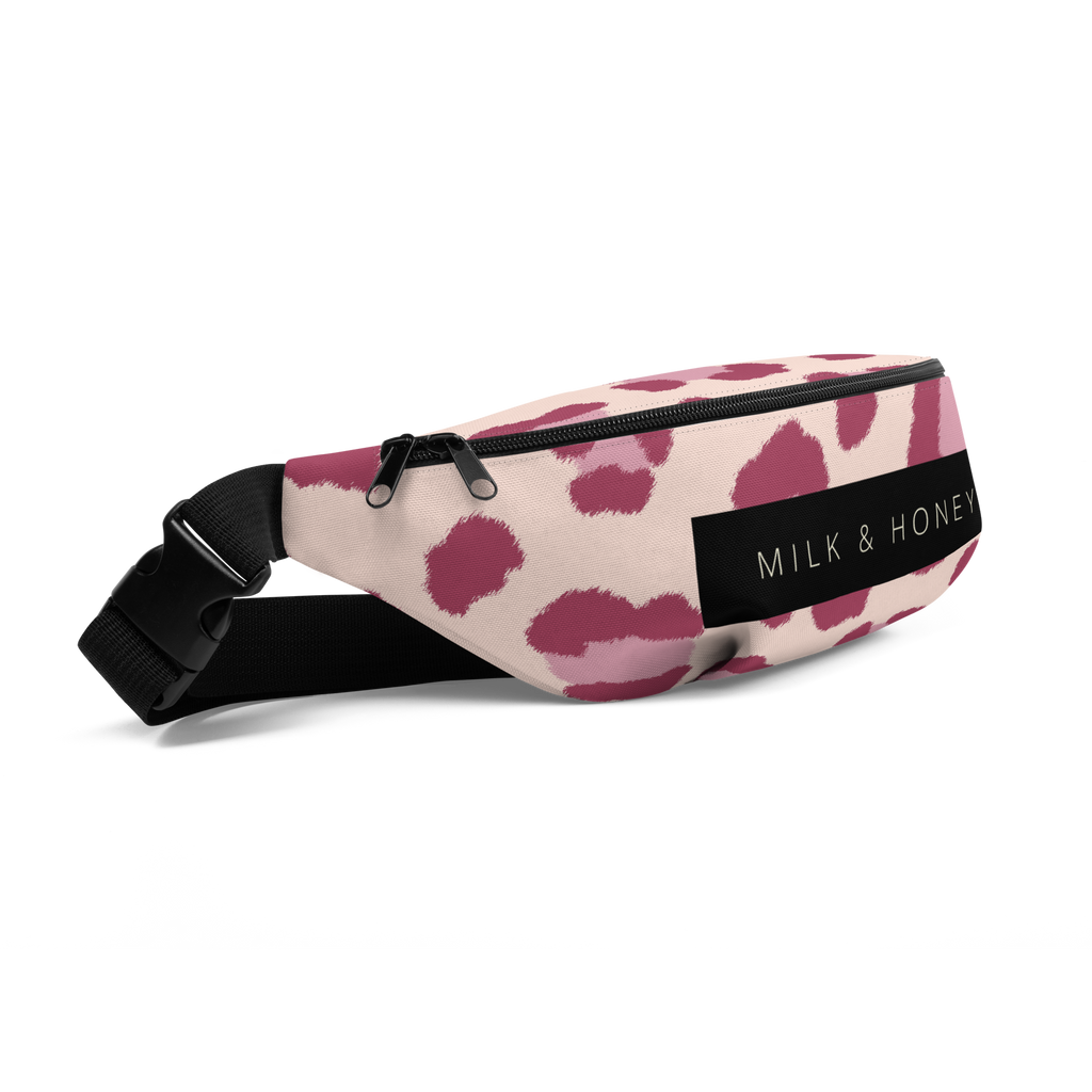 Corner of pink-spotted fanny pack with black dual-slider zipper, black strap and plastic buckle, and 'MILK & HONEY' label.