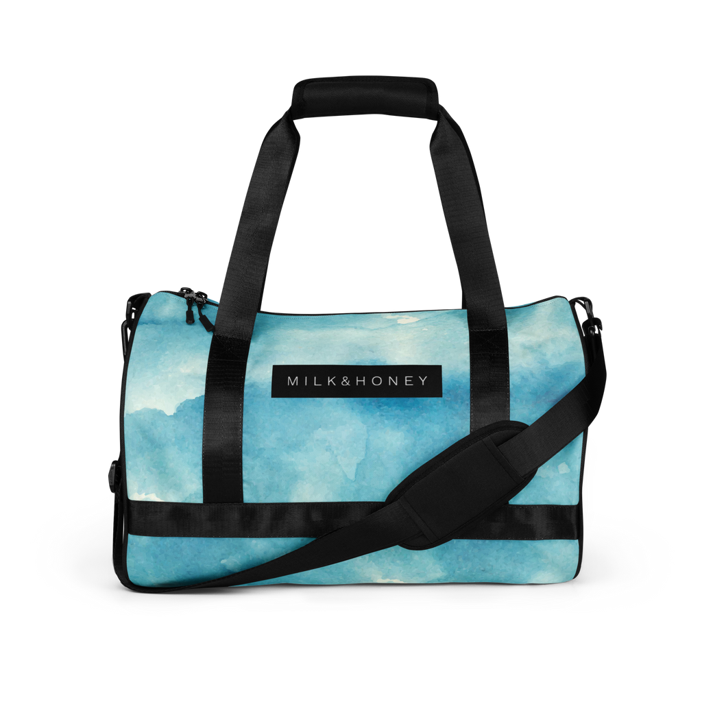 Black padded top handles and adjustable shoulder strap over a light blue watercolor duffel front with MILK&HONEY label