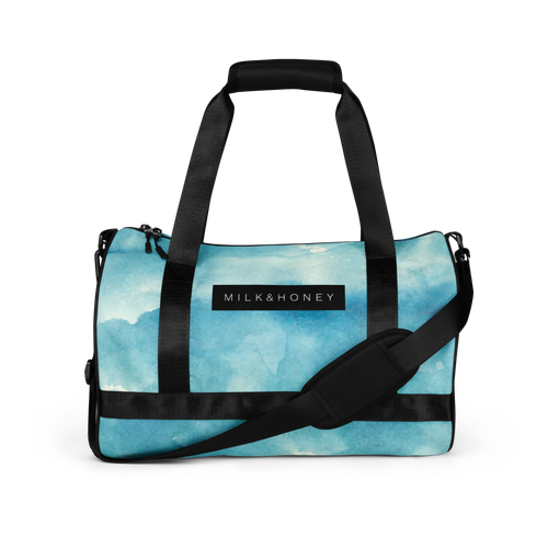 Black padded top handles and adjustable shoulder strap over a light blue watercolor duffel front with MILK&HONEY label