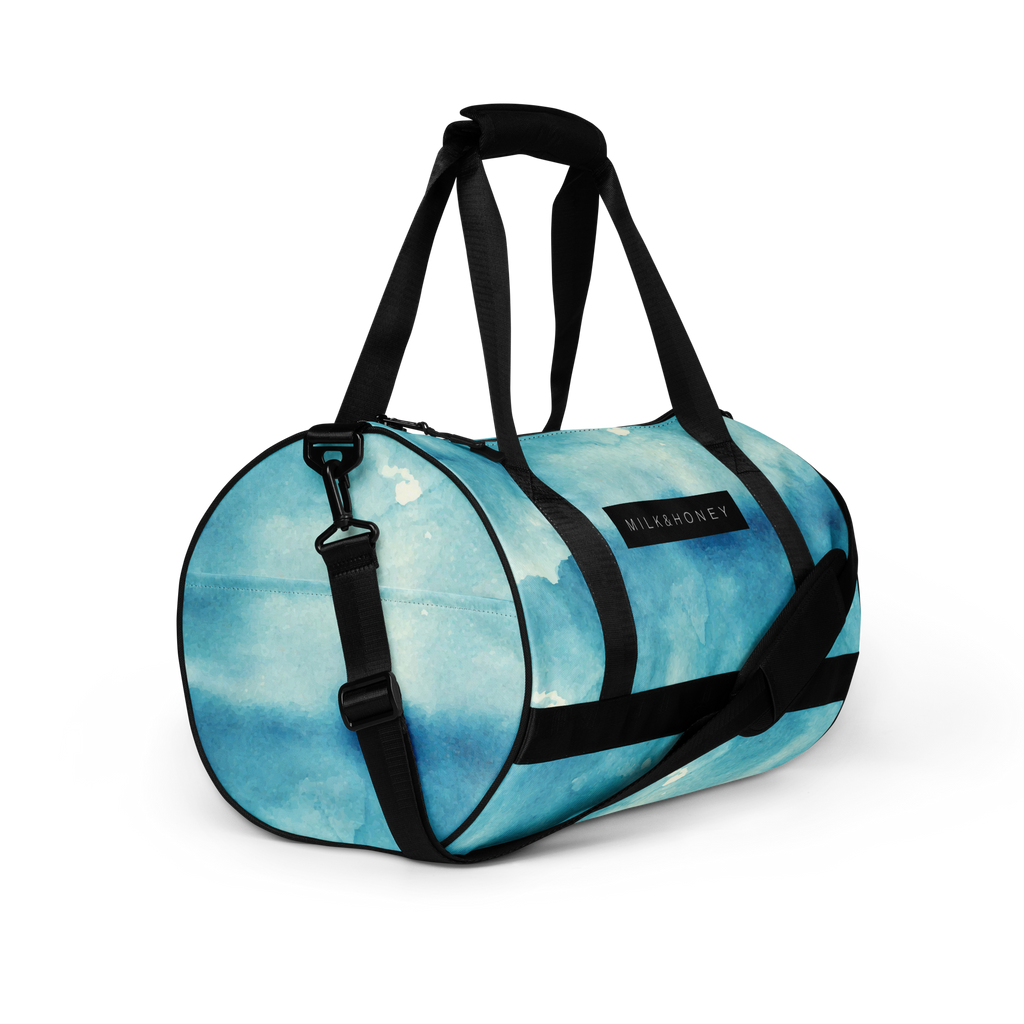 Blue watercolor-pattern duffel with black padded handles, adjustable shoulder strap, metal clip and a rectangular…