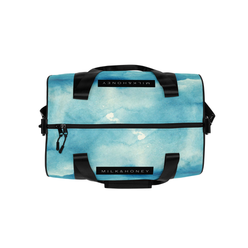 Top front of duffel with blue watercolor print, black padded handles, front zipper with dual pulls and 'MILK&HONEY' label