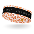 Headband with orange leopard spots on pale background, black center band reading MILK&HONEY, small yellow logo tag