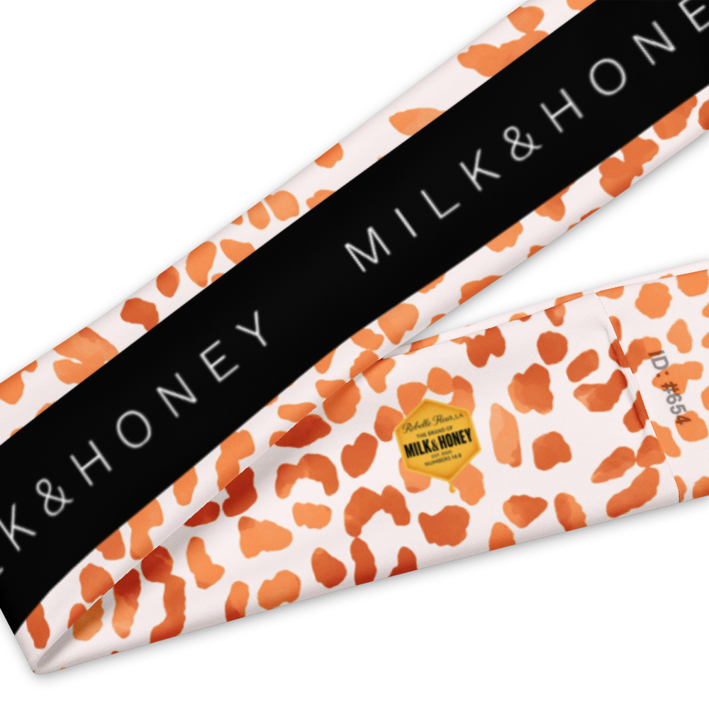 Headband with orange spotted pattern, black band reading MILK & HONEY and small yellow hexagon tag