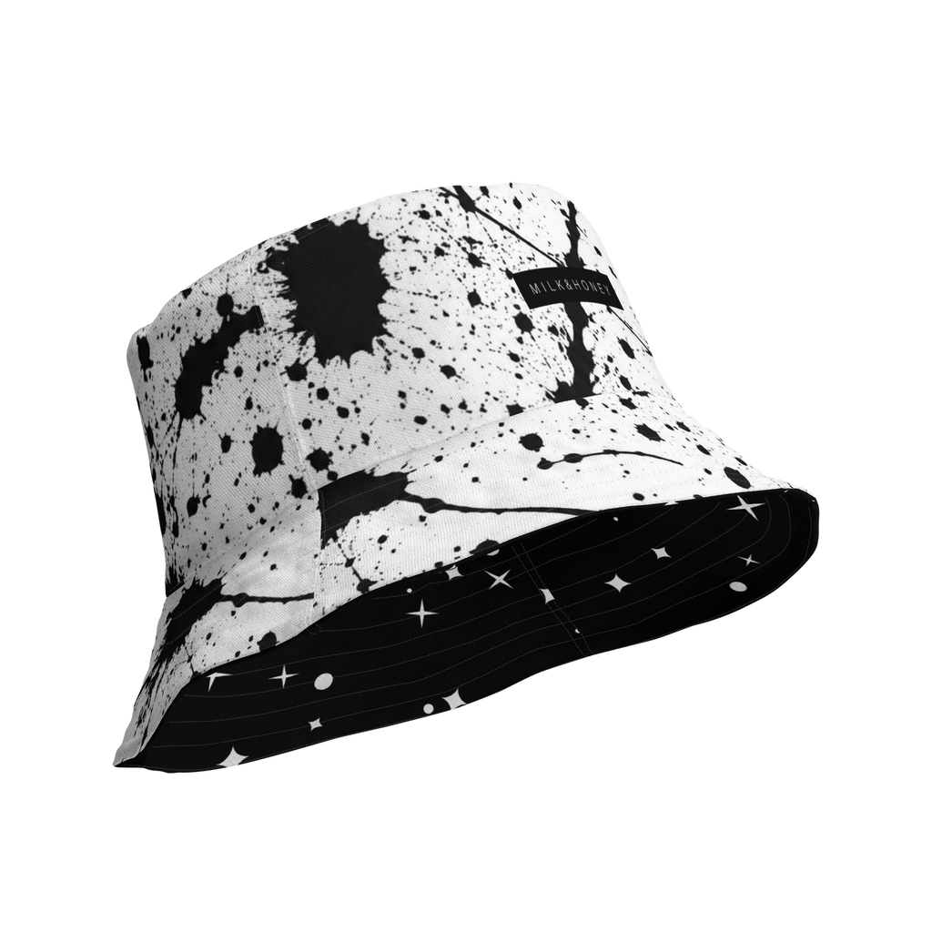 White bucket hat with black paint-splatter print, black MILK&HONEY label, underside shows black fabric with white star…