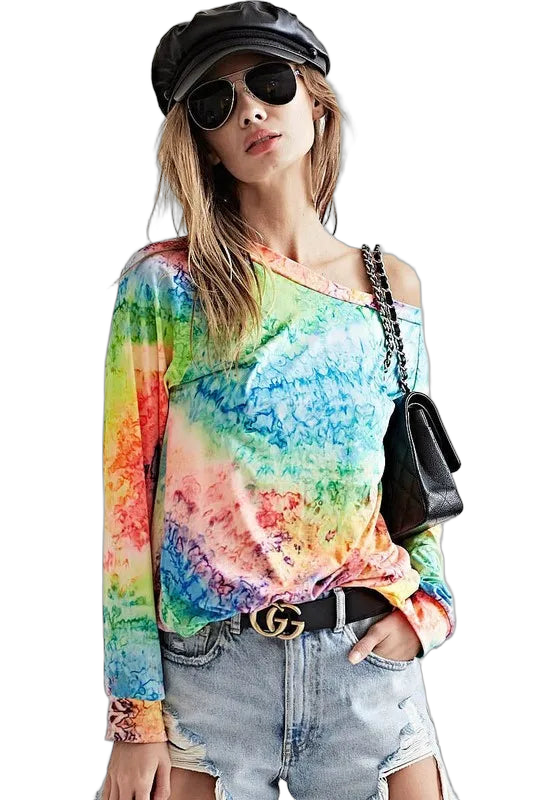 Woman in multicolor tie-dye long-sleeve knit top with one-shoulder neckline, denim shorts, belt, black cap and sunglasses