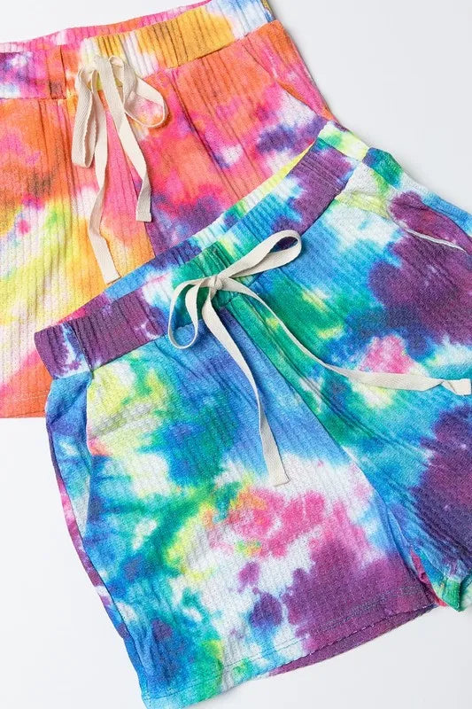 Two tie-dye casual shorts, blue-green and pink-orange, with cream drawstrings, elastic ribbed waists and side pockets.
