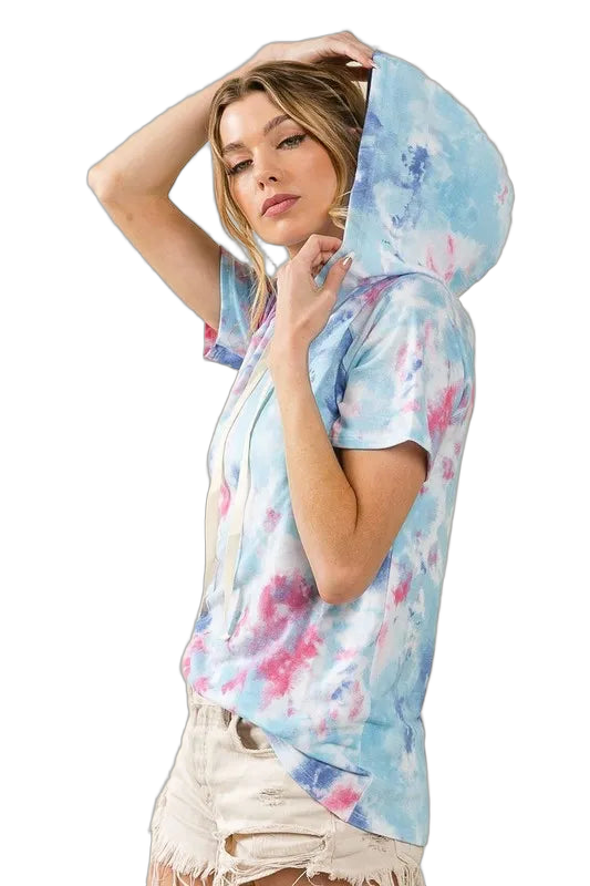 Woman wearing short-sleeve pastel blue and pink tie-dye hooded top with drawstrings; distressed light denim shorts.
