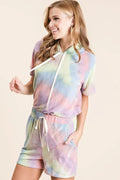 Woman wearing pastel tie-dye short-sleeve hoodie top and matching shorts with drawstring waist and side pockets, smiling