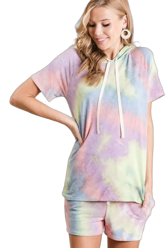 Model wearing pastel tie-dye short-sleeve hoodie with drawstrings and matching shorts, hand in shorts pocket